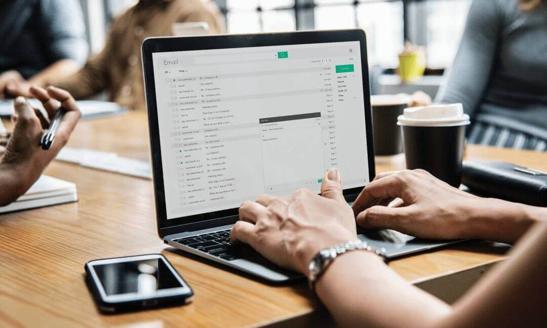 Somebody writes an email on a laptop during a group meeting in an office.